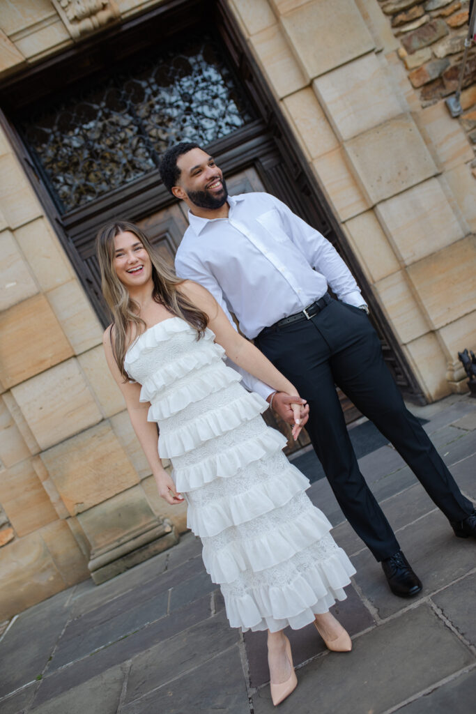 Man and woman laugh while holding hands as they stand in front of Graylyn Estate.