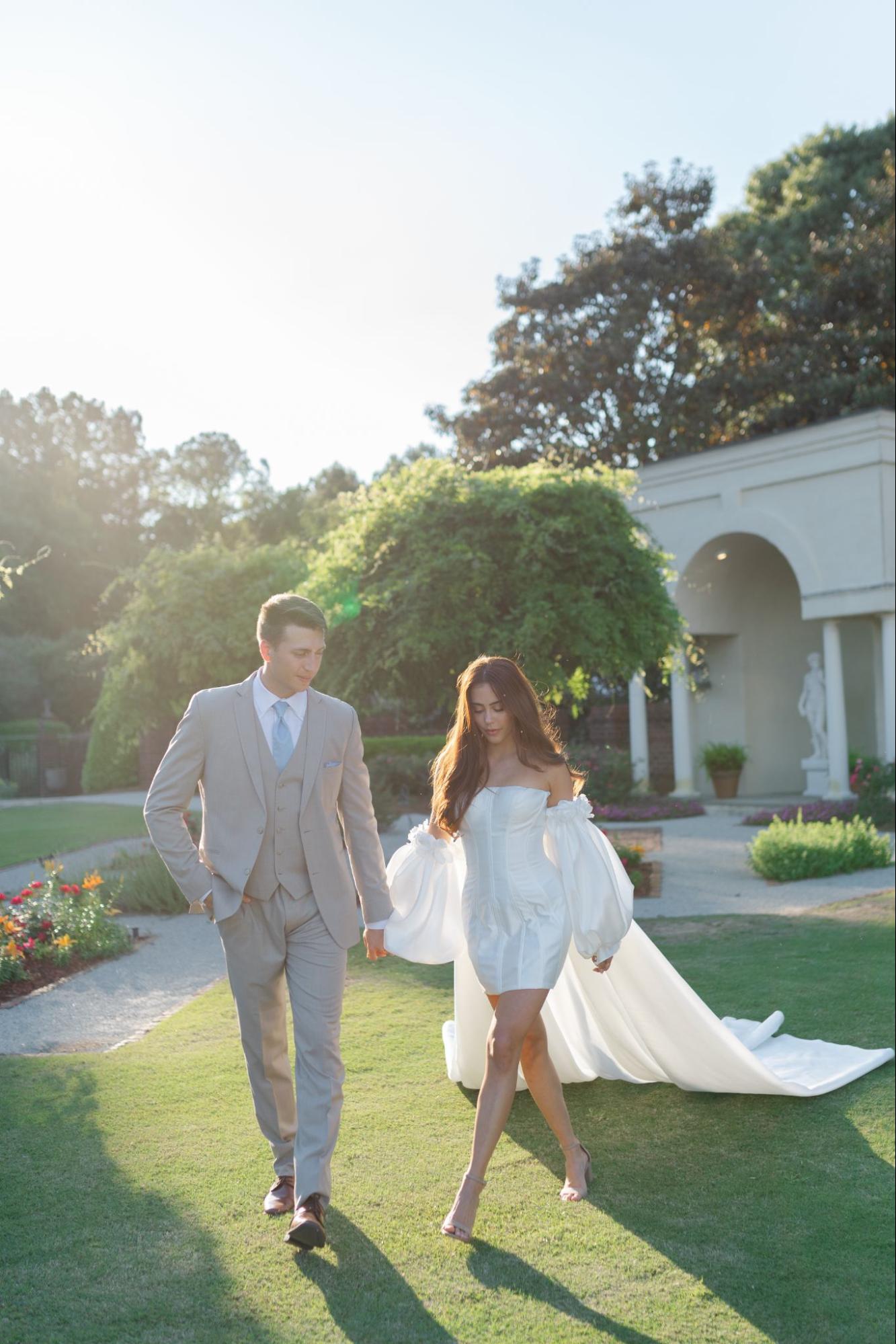 Bride and groom walking hand-in-hand through the lush gardens of Britton Manor on a sunny day.