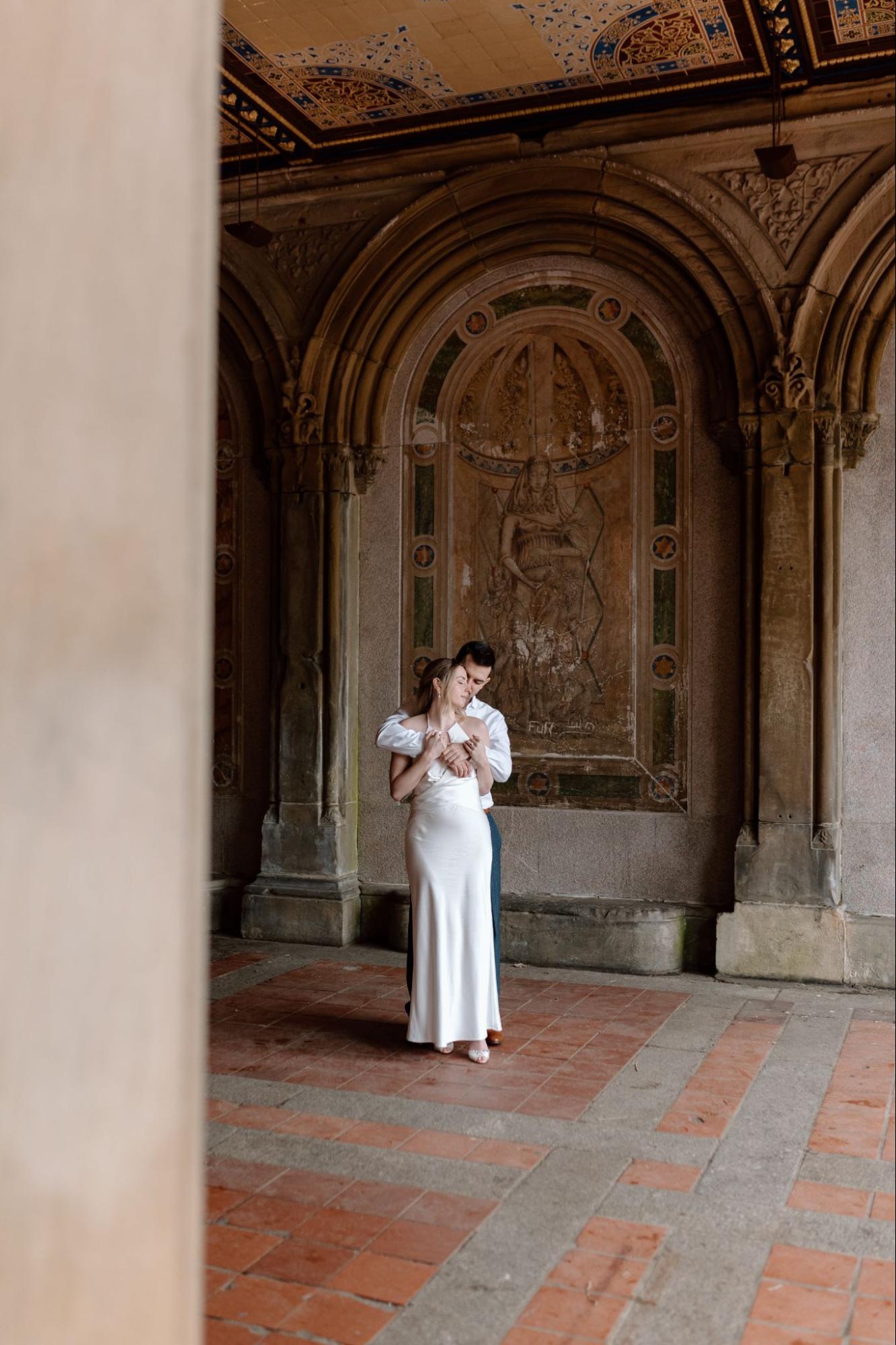 Couple in a tender embrace inside a sunlit alcove at Bethesda Terrace, Central Park, reflecting the romance of the city.