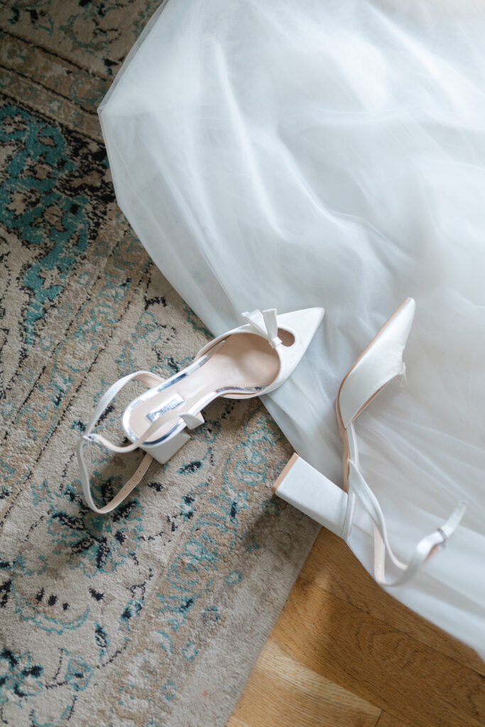 A pair of the bride's white shoes lay on the ground intermingled with her dress on the floor.