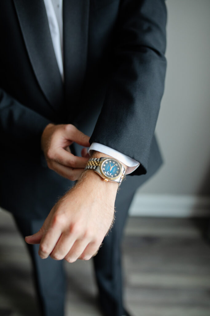 The groom's watch, which is gold and silver, on his wrist as the groom adjusts the cuff of his suit jacket.