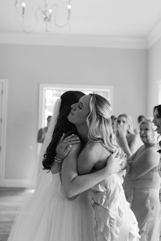 One of the bridesmaids hugs the bride, smiling and closing her eyes as she embraces her.