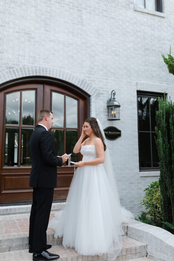 The bride wipes a tear from her eye as she stands before the groom reading her vows to him in front of The Bradford.