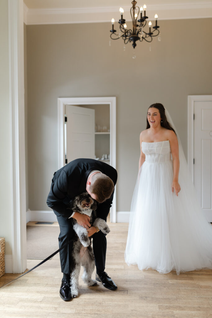 The bride laughs as the groom plays with their puppy inside the main house at The Bradford.