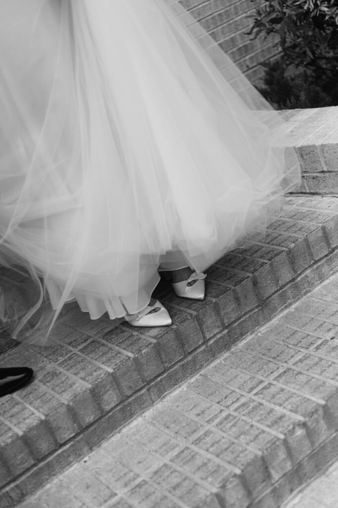 The bride's beautiful white shoes with bows peep out from under her dress as she walks down a flight of stairs.