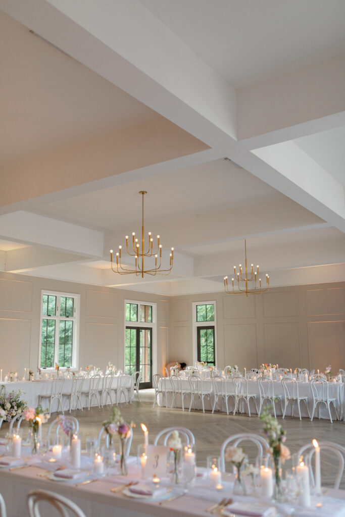 Inside the main ball room at The Bradford in New Hill NC white-clothed tables line the room in a square. The tables are adorned with candles, bud vases filled with flowers, plates, and other gorgeous details.