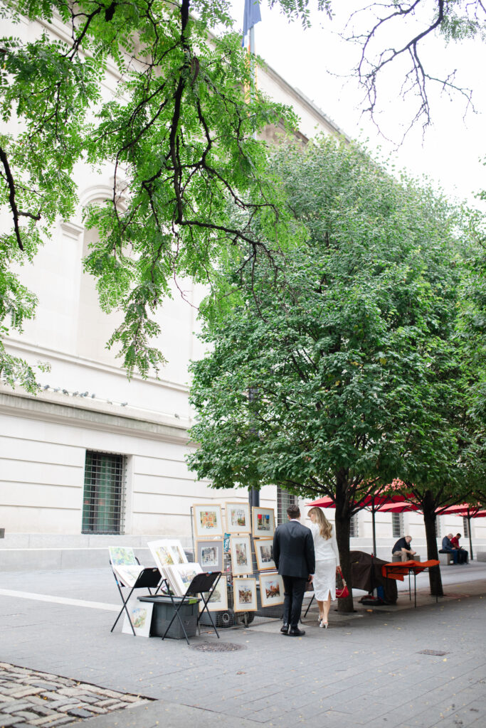 A man and woman browse through a vendor's paintings they are selling outside The MET.