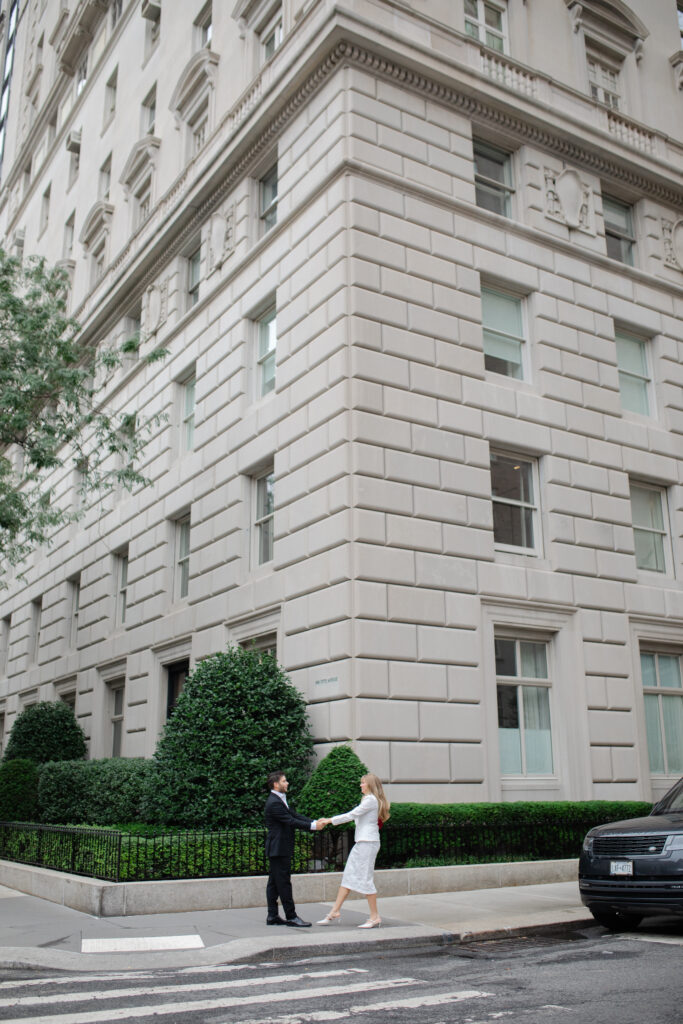 Man and woman hold hands and dance together on a street corner in NYC, just outside the MET.