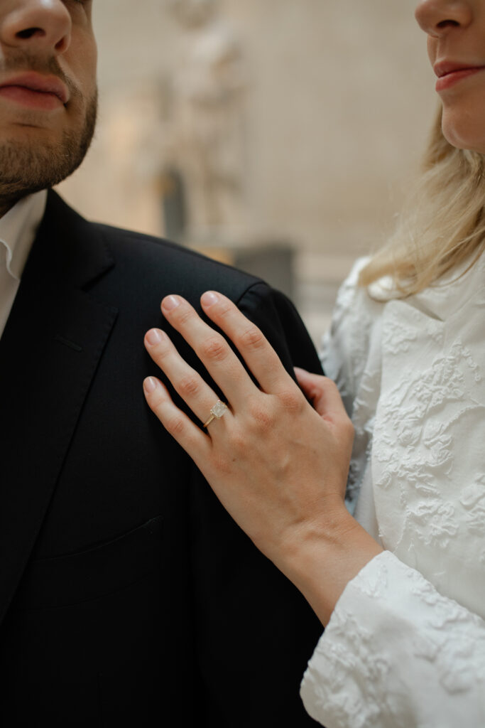 A close up of the woman's engagement ring. It's on a square cut diamond on a gold band.